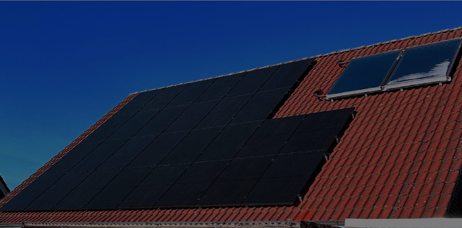 Rotes Dach mit Photovoltaikanlage und Warmwasser mit blauem Himmel