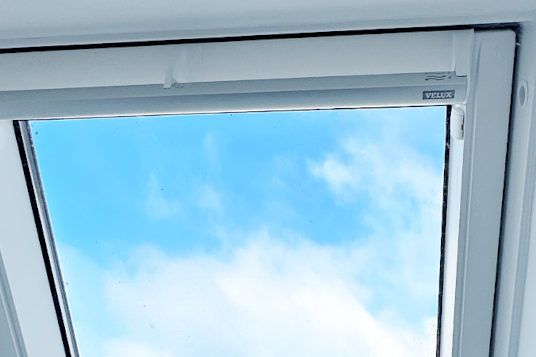 modernes Thermo-Dachfenster mit Velux Rollo mit blauem Himmel